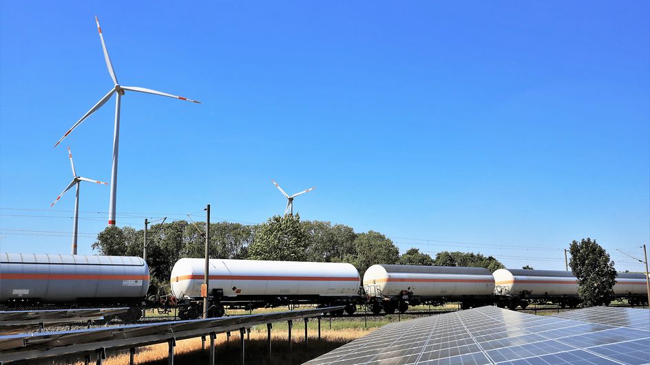 Zielony krajobraz z turbinami wiatrowymi, instalacjami solarnymi i przejeżdżającym pociągiem