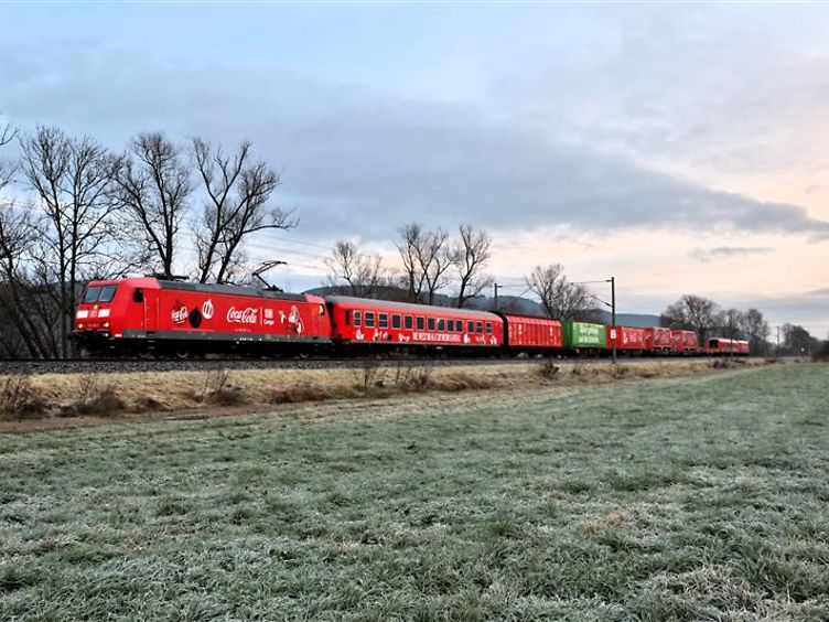 Rot gestalteter Güterzug mit Coca-Cola-Werbung auf einer Bahnstrecke durch eine winterliche Landschaft.